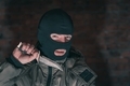 A thug in a balaclava with a knife against a brick wall in the dark shows threatening gestures - PhotoDune Item for Sale