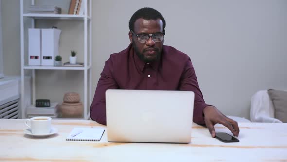 African Man Work at Office with Laptop Take Smartphone and Search Information Online Spbas