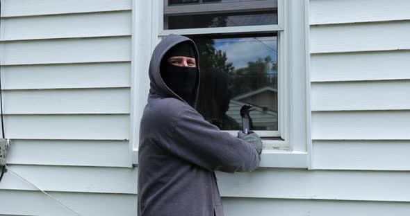 Burglar pries open a window with a crowbar and starts to climb into a home