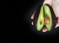 One hand holding halved avocado against the black background  - PhotoDune Item for Sale