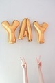 Golden foil balloons in words YAY. Two hands against the white background. Celebration time. - PhotoDune Item for Sale