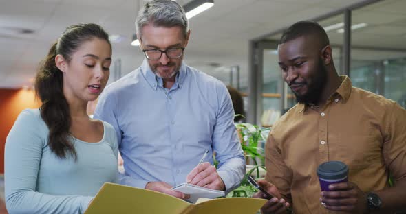 Diverse male and female business colleagues talking and holding documents