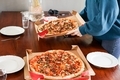 Two big pizzas has been delivered and woman serving them on the table.  - PhotoDune Item for Sale