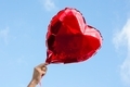 Hand holding red foil balloon in the heart shape against the blue sky.  - PhotoDune Item for Sale