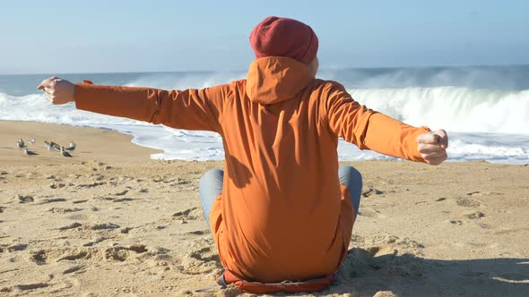 Man Sits on Beach with Portable Computer and Stretches Arms