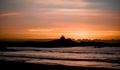 Dramatic golden sunset of two men admiring the view on vacation, standing on a large rock on a beach - PhotoDune Item for Sale