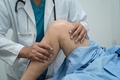 Asian doctor physiotherapist examining, massaging and treatment knee and leg of senior patient in or - PhotoDune Item for Sale