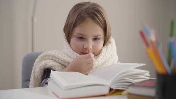 Close-up Portrait of Charming Caucasian Girl Sitting with Book in White Scarf and Sneezing. Ill