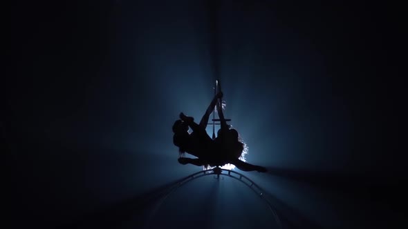 Two Girls Rotating on a Metal Hoop in Dark Room . Black Smoke Background. Silhouette. Slow Motion
