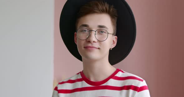 Portrait of a young unusual man in a hat and glasses. Hipster student designer lookung at camera.