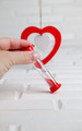 female hand holding an hourglass on the background of a red heart - PhotoDune Item for Sale