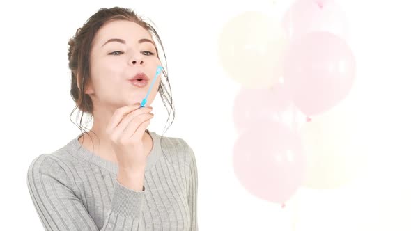 Attrctive Young Caucasian Girl with Brunette Hair Blowing Soap Bubbles Standing on White Background