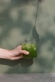 Female hand holding glass of matcha against green wall with plant shadows.  - PhotoDune Item for Sale