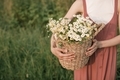 A girl in a sundress in a field holds a wicker basket full of flowers. - PhotoDune Item for Sale