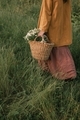 Aesthetic shot of woman in pastel color clothes walking with basket with field flowers in nature.  - PhotoDune Item for Sale