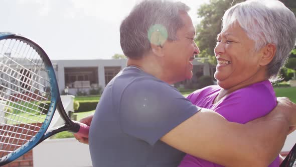 Video of happy biracial senior couple embracing and kissing after after match on tennis court