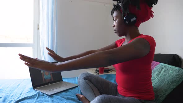 Young woman sitting on bed during video call teaching to meditate