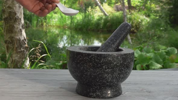 Hand is Putting the Sea Salt in the Grey Stone Mortar in Slow Motion Outdoors