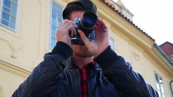 A Young Handsome Man Takes Photos with a Camera - Closeup From Below - a Yellow Building