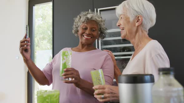 Happy senior diverse women drinking healthy drink in kitchen at retirement home