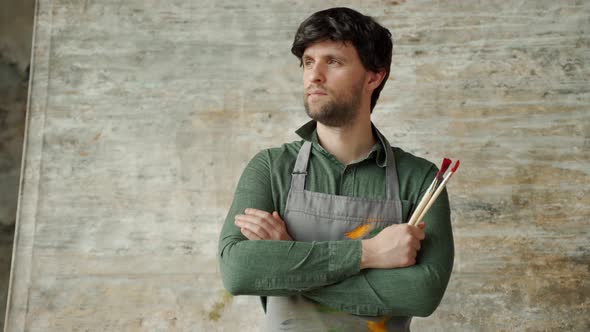 Portrait of a Contented Young Male Artist Crossing His Arms with a Brush in His Hand on a Background / Videohive