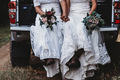 Two brides sitting in the back of a truck wearing boots and holding bouquets  - PhotoDune Item for Sale