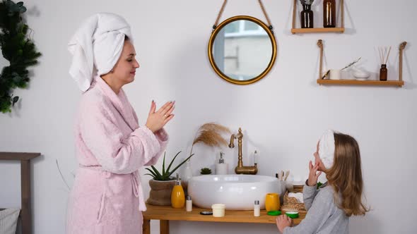 Woman with Little Daughter Applies Creme on Faces