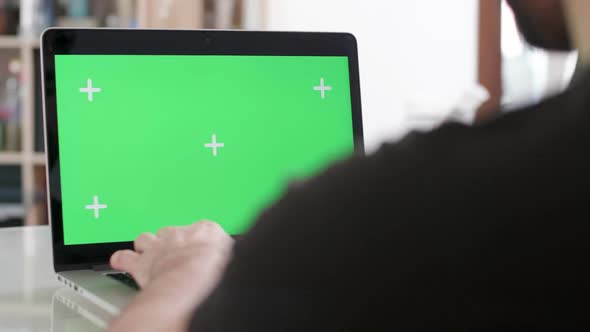 Slider Shot Over the Shoulder of a Man Working on His Laptop with Green Screen on