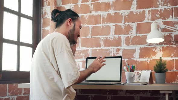 Asia guy speaks on mobile phone and working on laptop in living room at house in the morning.