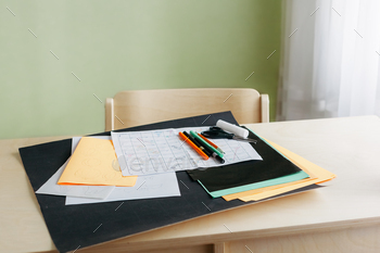 Sheets of colored paper, sketches of a board game, colored pens and scissors on desk