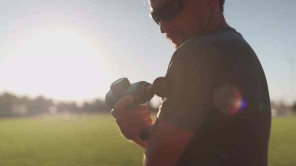 Athletic Male Massages Muscles with Hand Massage Gun Recovering From Stadium Running Workout