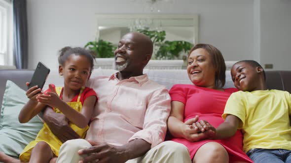 Happy african american grandparents and grandchildren sitting on sofa, taking selfie