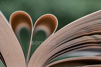 Closeup macro of a book with pages folded like a heart on green background