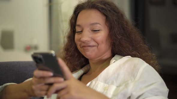 Young Woman Brunette in Shirt Reads Message on Smartphone