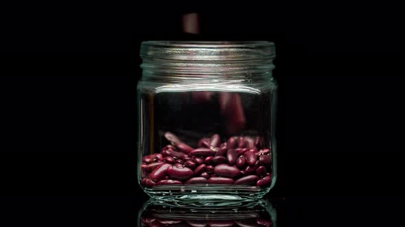 Closeup of Falling Down Red Beans Into Glass Jar on Black Background