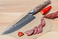 Sharp chef's knife close up on the cutting board and sliced smoked sausage. - PhotoDune Item for Sale