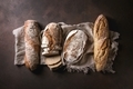 Variety of loafs fresh baked artisan rye and whole grain bread on linen cloth over dark brown - PhotoDune Item for Sale