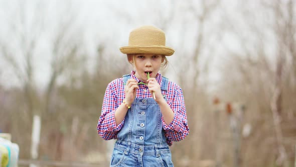 a Funny Little Girl in a Hat Eats Green Onions and Waves His Head in Pleasure