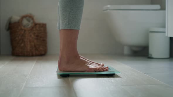 Legs of unrecognizable woman stepping on the bathroom scale. Shot with RED helium camera in 8K.