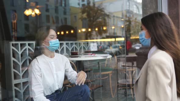 Two Women in Protective Masks Opposite Each Other Window Between Them
