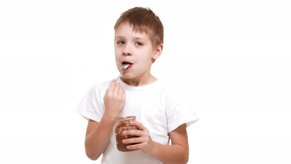 Elementaryschool Aged Caucasian Boy Eating Chocolate Spread with Great Pleasure Standing on White