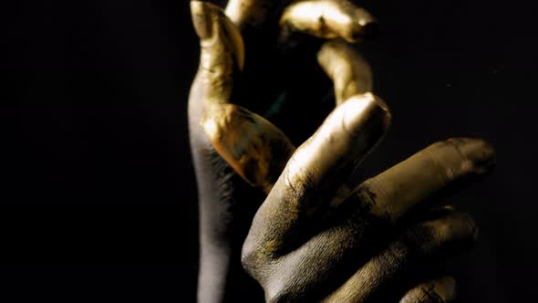 Closeup of the Black Hands of a Woman with Golden Fingers on a Black Background