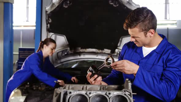 Male mechanic checking a car parts while female mechanic servicing a car