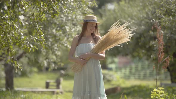 Cute Fashion Young Woman in Straw Hat and Long White Dress Looking at the Camera Smiling