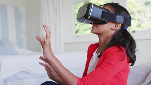 Mixed race girl sitting at home on sofa playing wearing virtual reality glasses