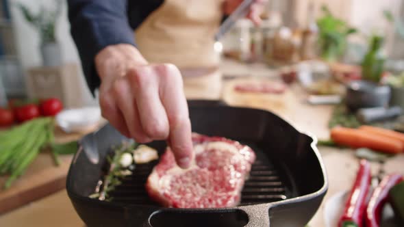 Male Cook Adding Salt to Meat Steak on Grill Pan