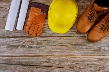 ints in the set of protective workwear yellow hard hat protective gloves waterproof working boots on wooden background.