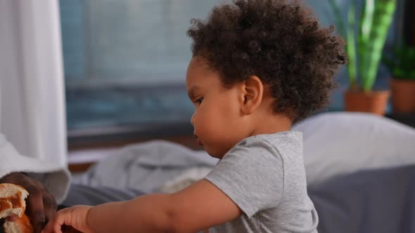 Side View Portrait of Curios Charming African American Little Boy Eating Croissant Resting with