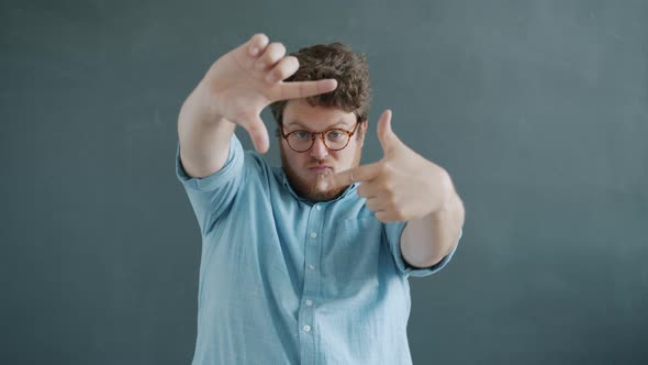 Slow Motion of Guy Making Focus Hand Gesture and Smiling Looking at Camera on Gray Background