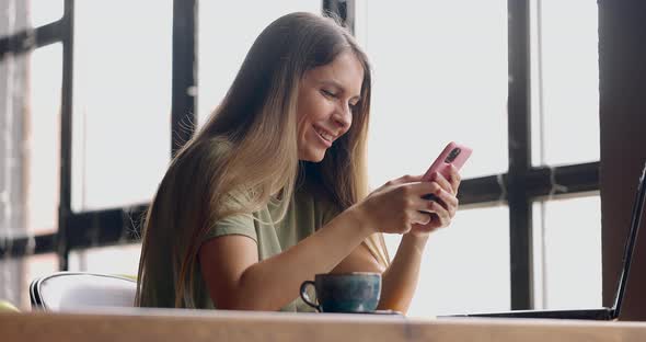 Young Woman with Long Hair Chatting Using Smartphonelaughing While Having a Cup of Coffee in Cafe